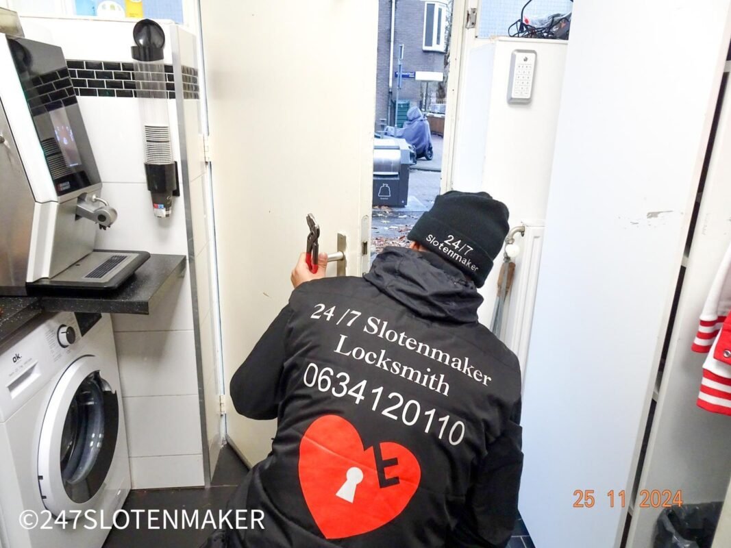 Een slotenmaker met donkere jas buigt zich voorover om een slot te openen in een Amsterdamse woning