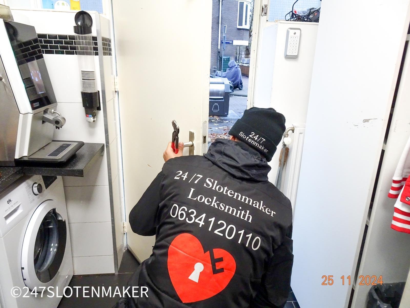 Een slotenmaker met donkere jas buigt zich voorover om een slot te openen in een Amsterdamse woning