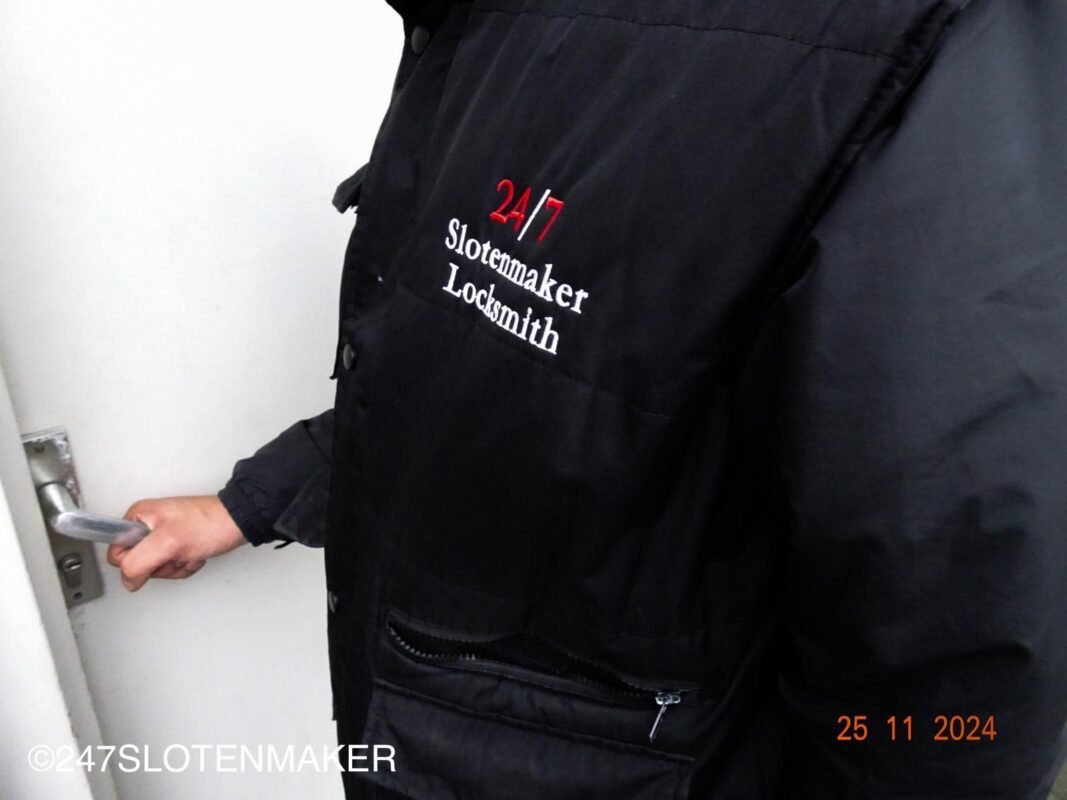 Een slotenmaker met zwarte jas werkt voor een blauwe deur aan het slot