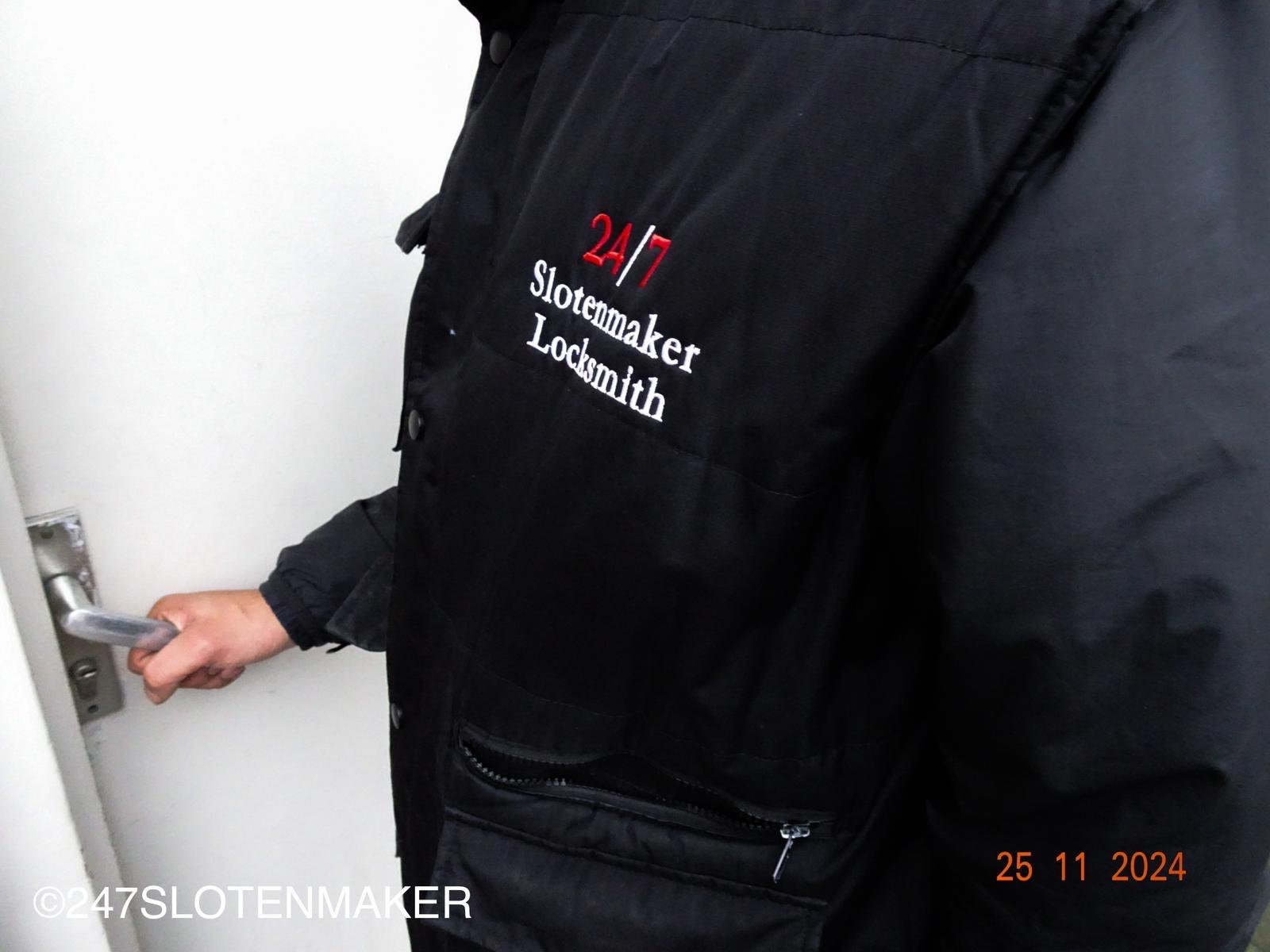 Een slotenmaker met zwarte jas werkt voor een blauwe deur aan het slot